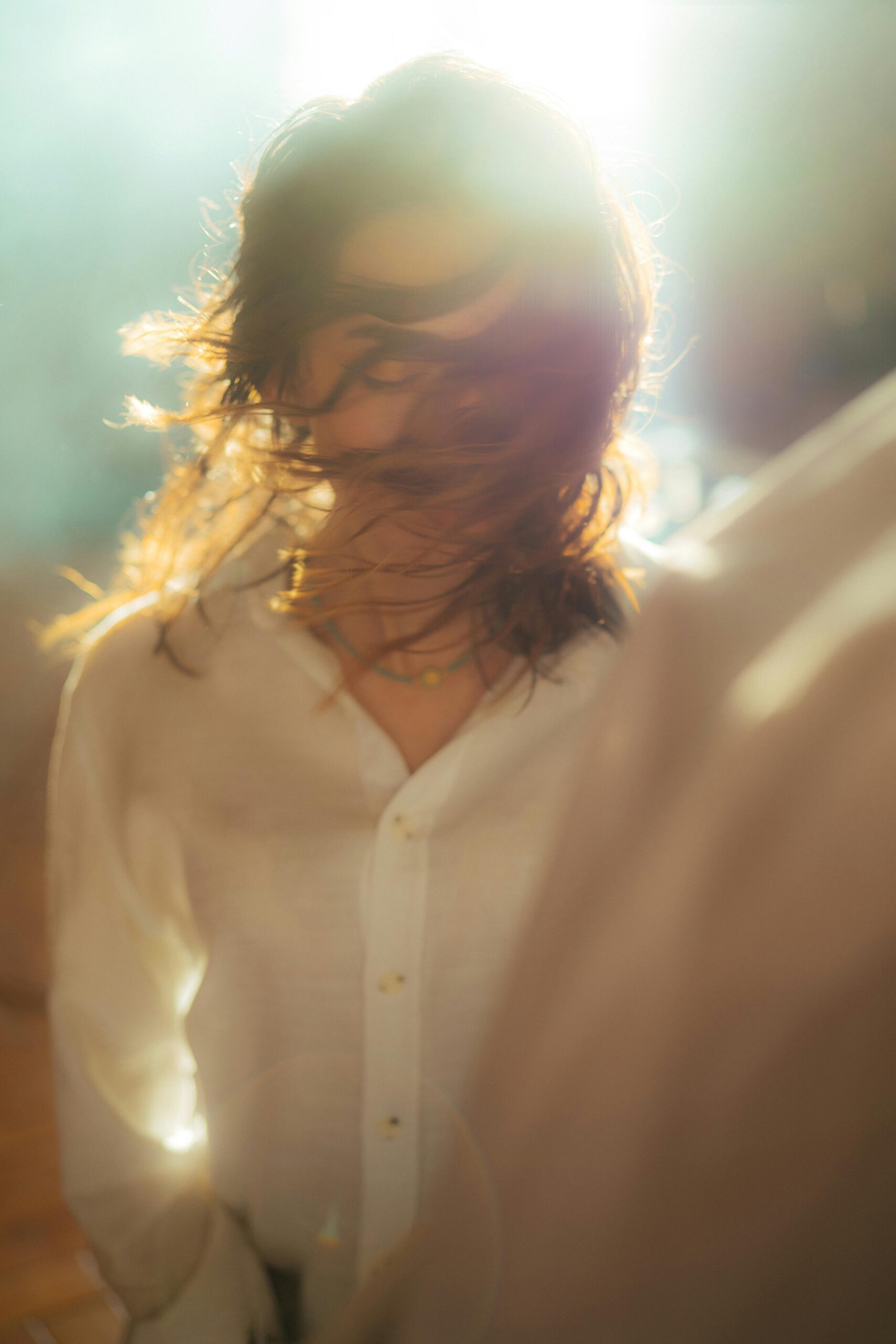 Artistic portrait of a woman with long hair illuminated by sunlight, creating a dreamy effect.