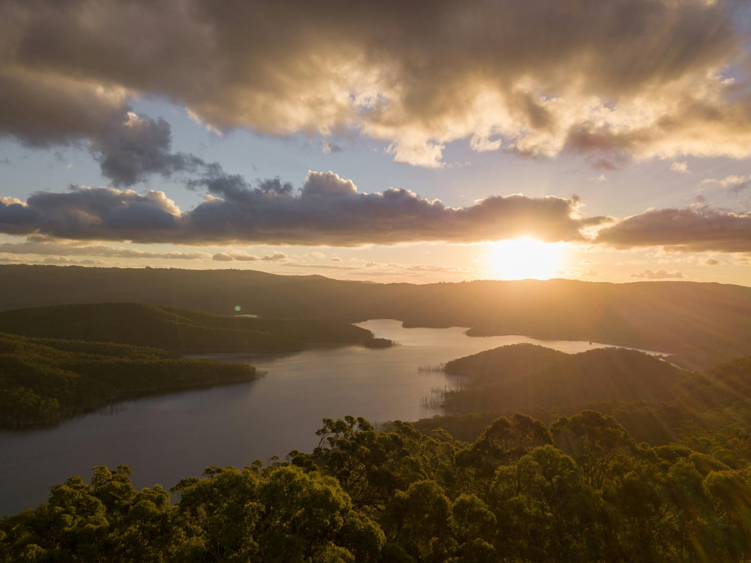 A stunning aerial panorama of Hinze Dam at sunset, showcasing serene water reflections and vibrant sky.