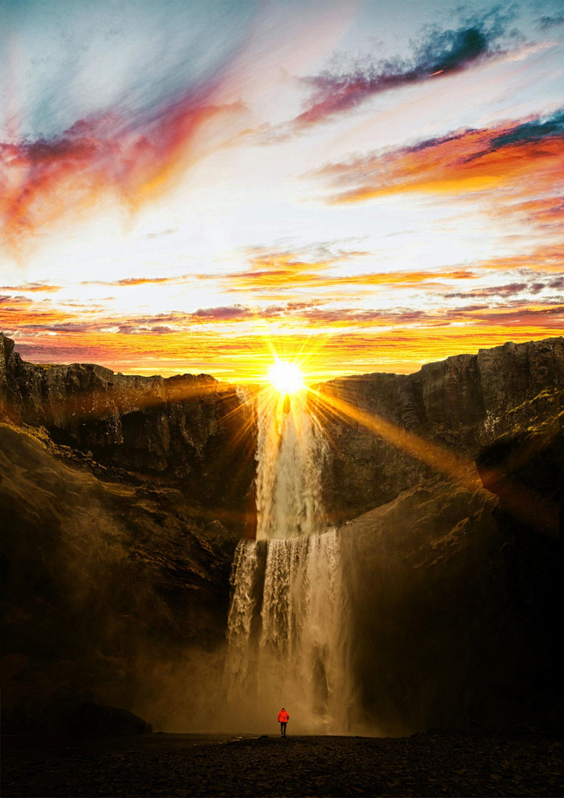A stunning sunset casting vibrant colors over a powerful waterfall surrounded by cliffs.